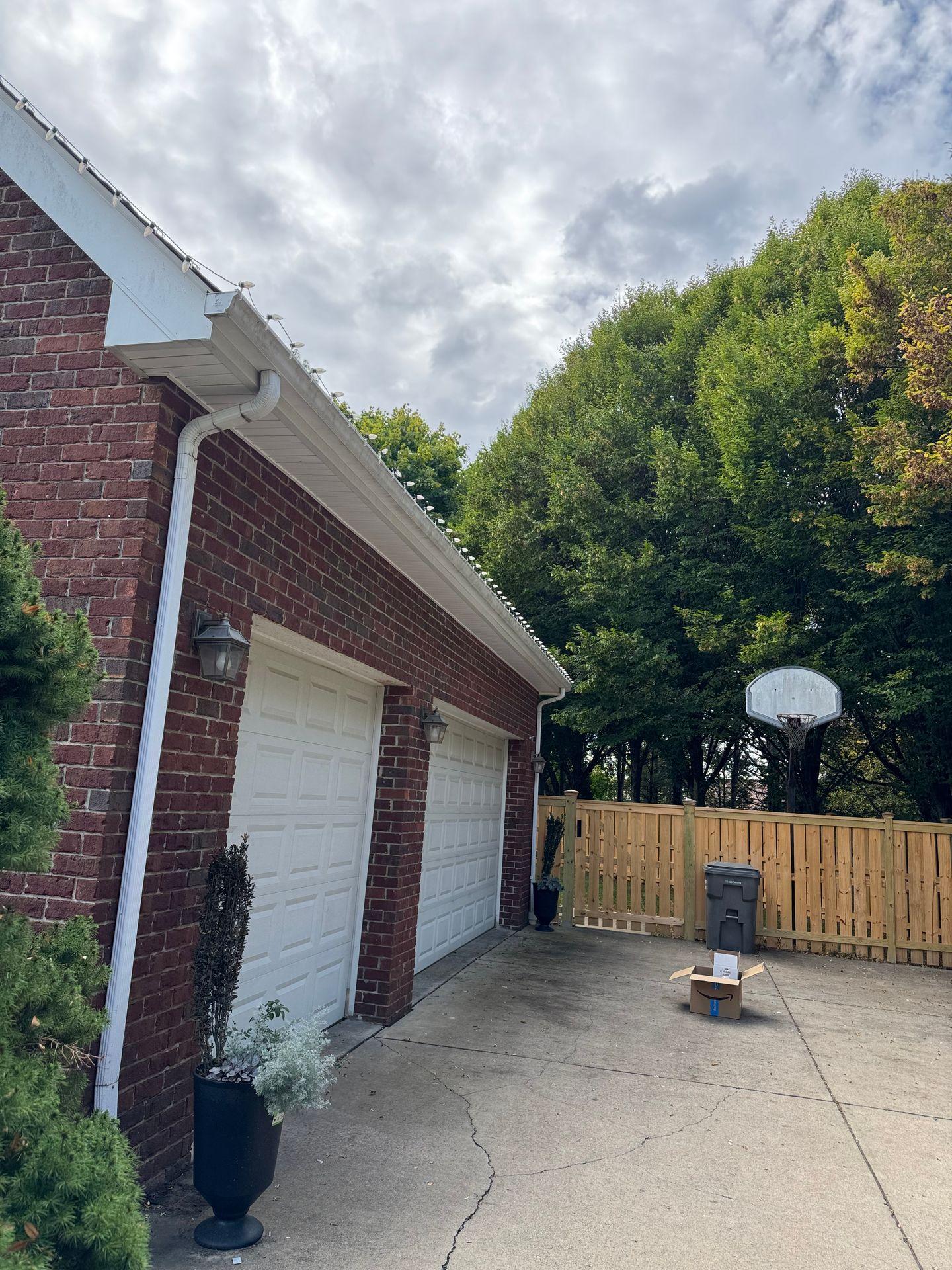 Brick home exterior with white garage doors and driveway with green trees.