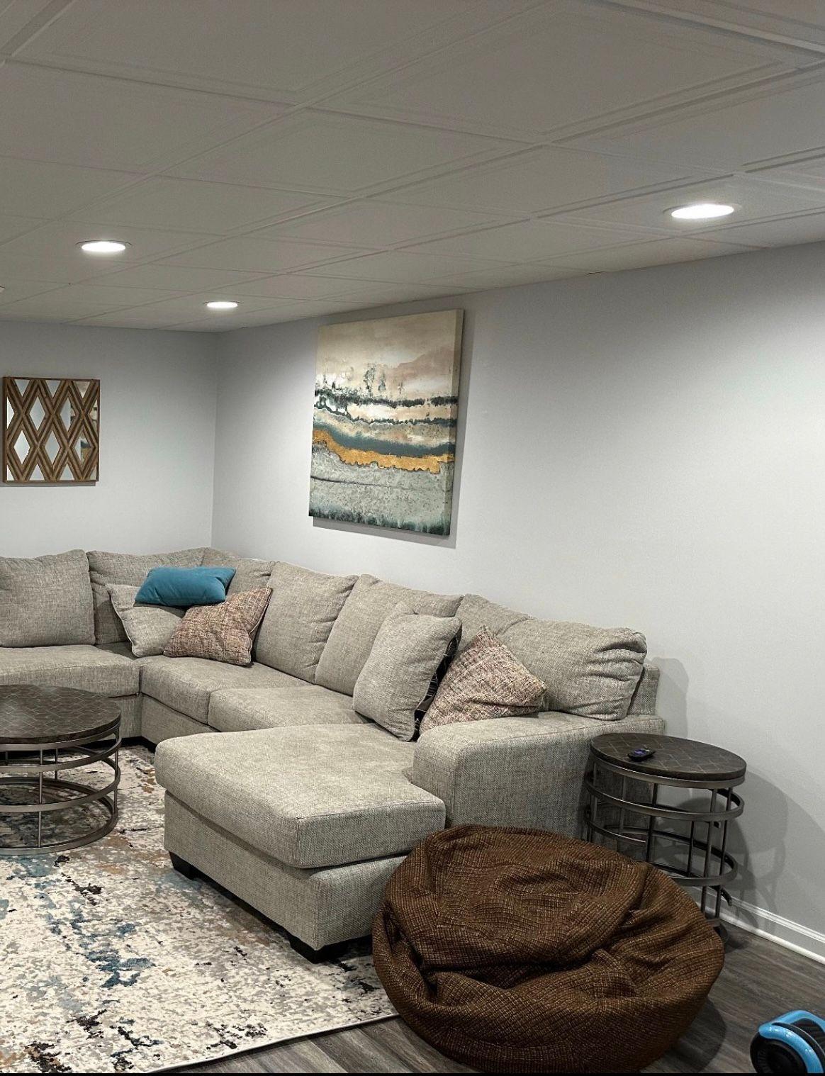 Cozy basement living room with gray sectional sofa, abstract wall art, and circular coffee tables.