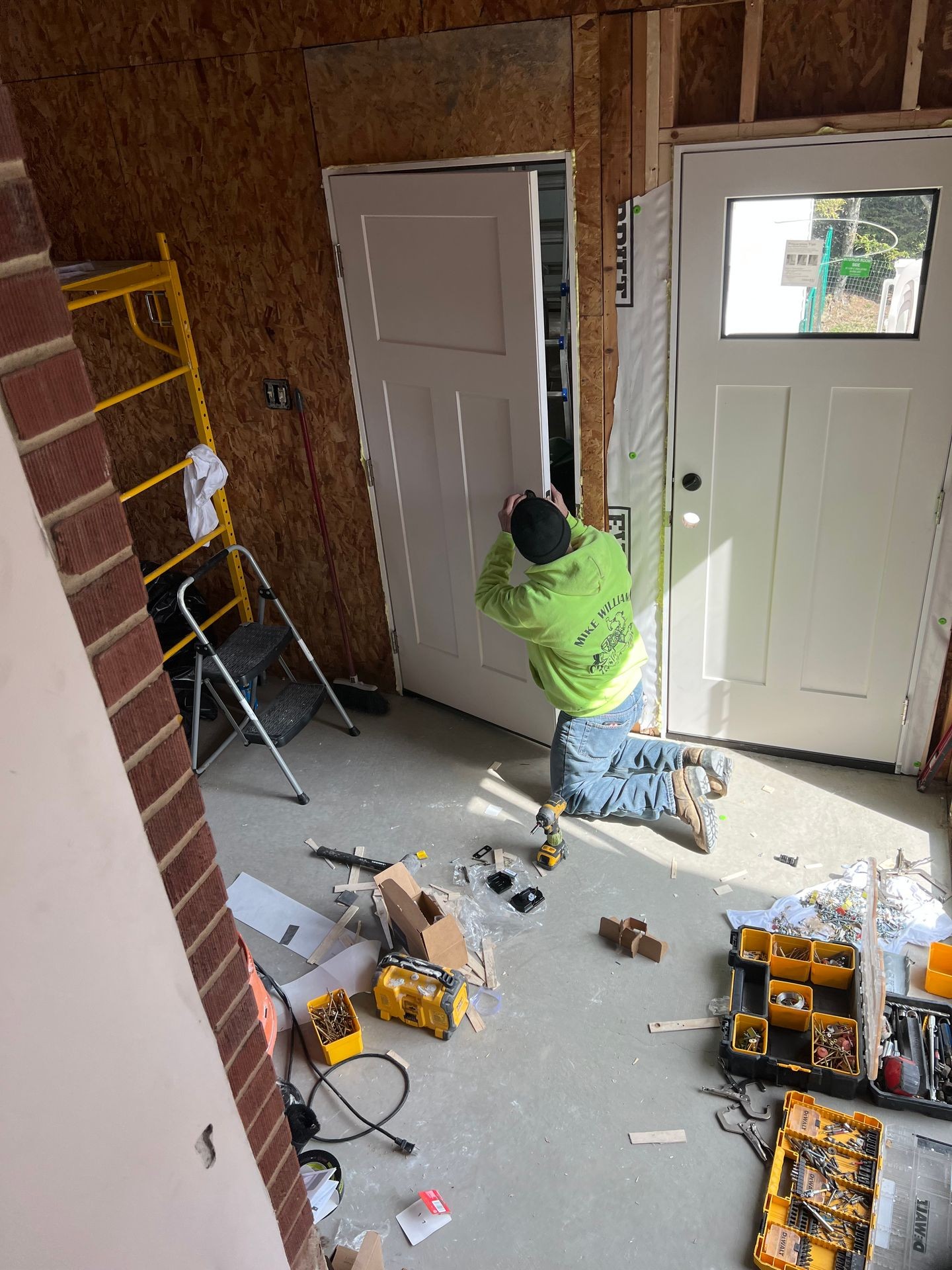 Person installing a white door frame inside a room with tools and materials scattered on the floor.