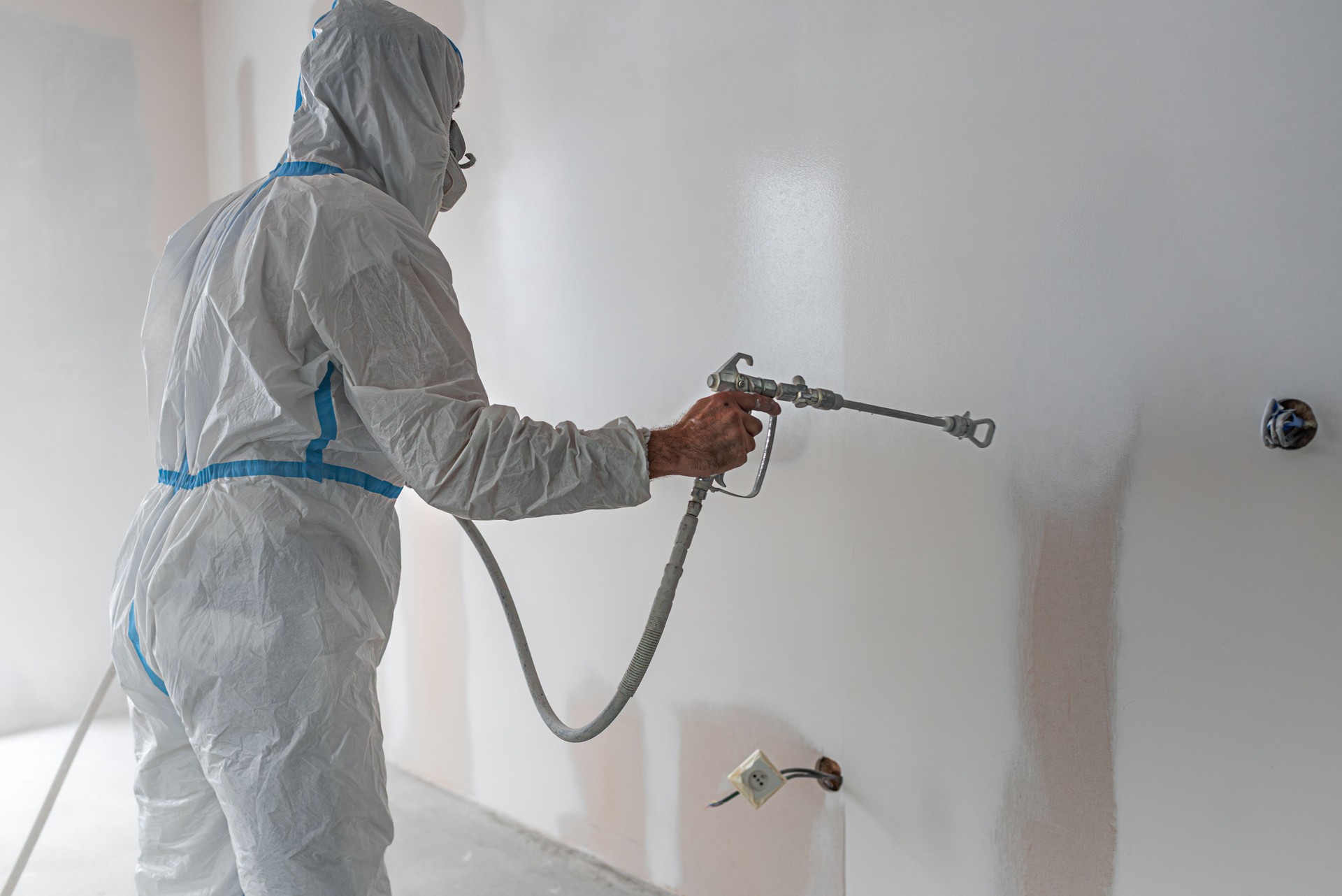 Spray painting walls. Painter wearing protective overalls while painting interior walls with a sprayer.