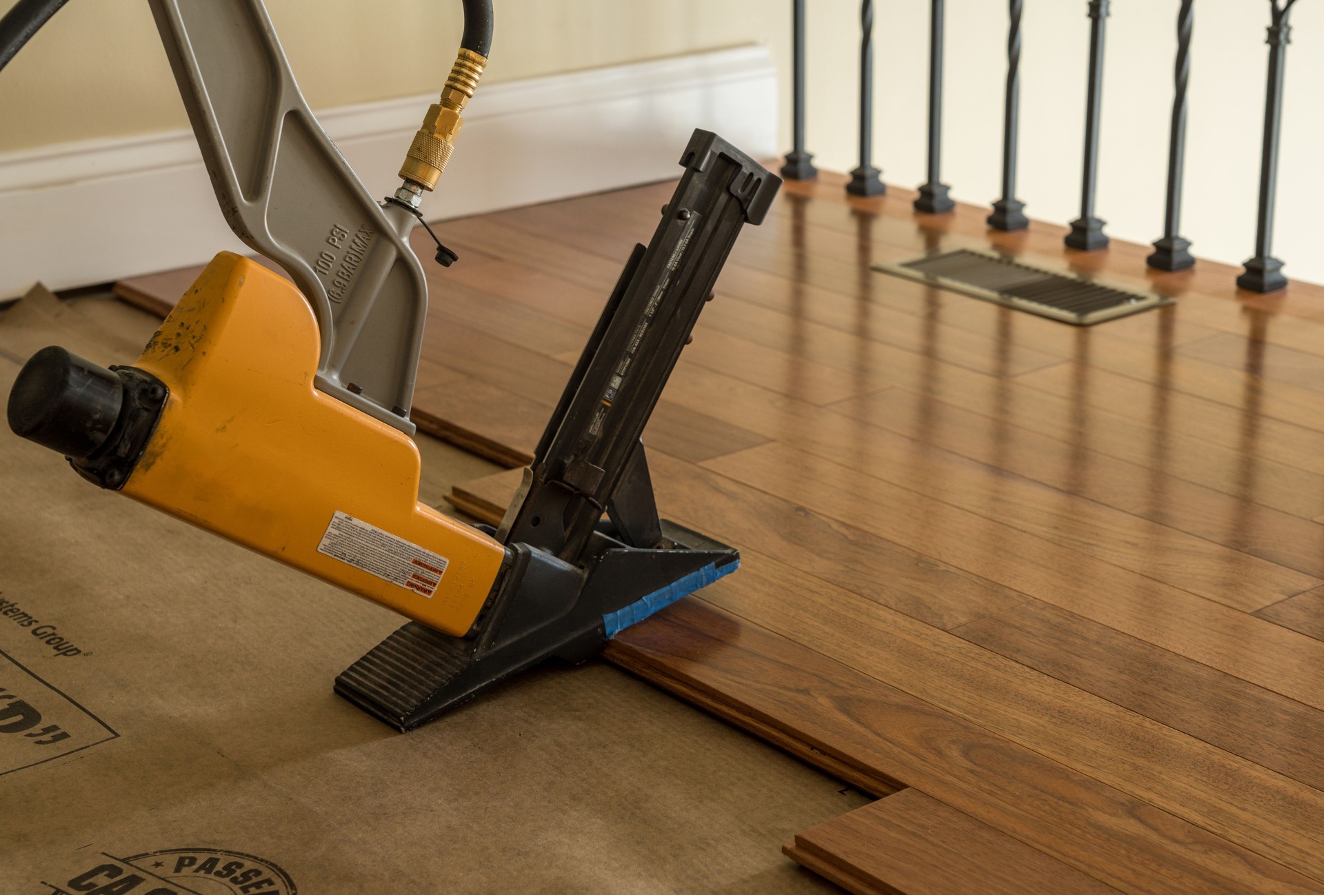High pressure nail gun ready to install sections of Brazilian Cherry hardwood flooring