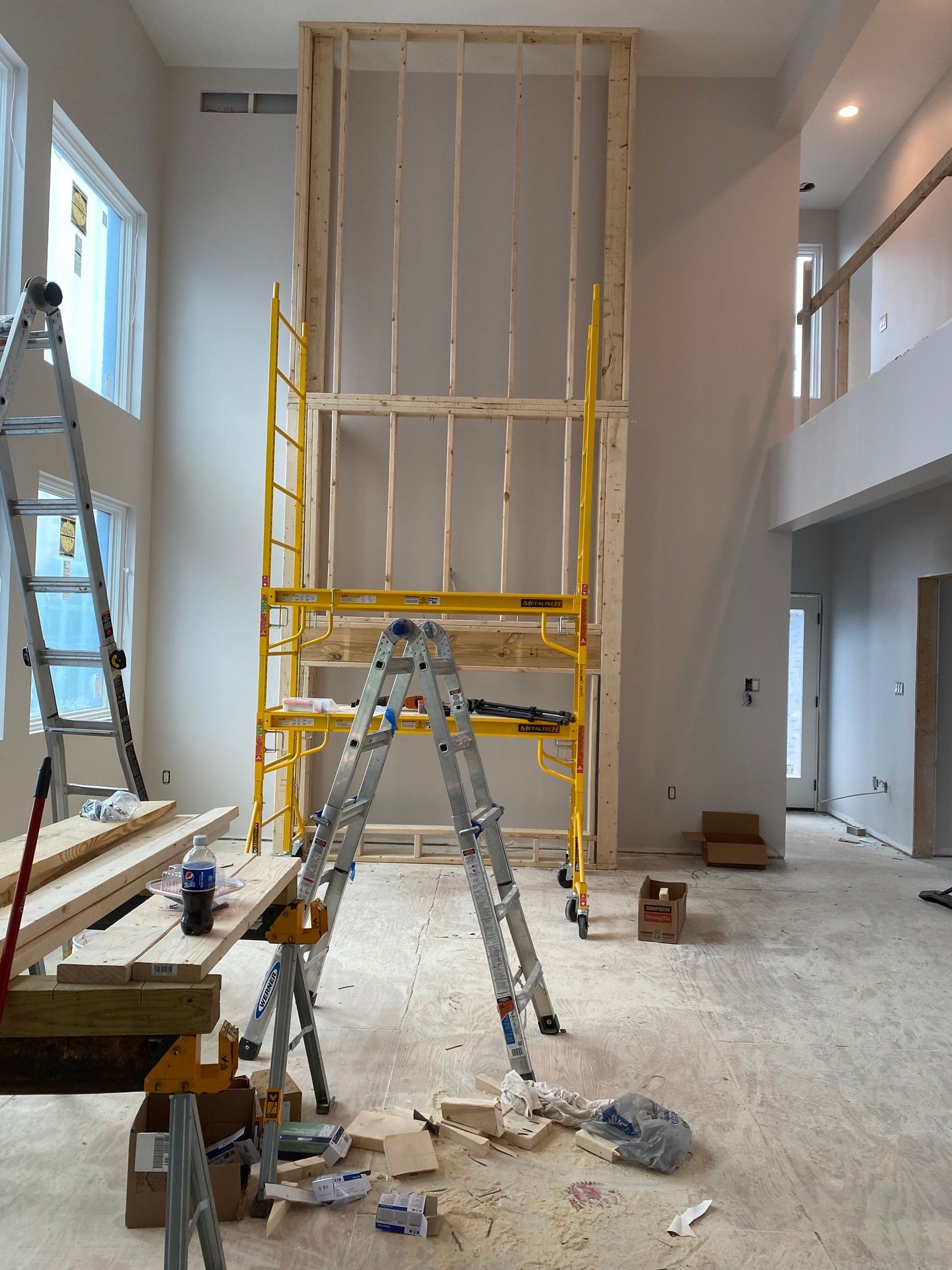 Interior construction site with ladders, scaffolding, and wooden framework under a high ceiling.